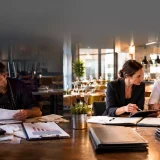 Restaurant owner reviewing financial reports with a restaurant consultant discussing strategies to prevent restaurant failure and improve profitability.