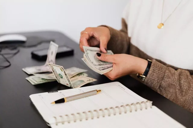 A person counting money next to a black desk