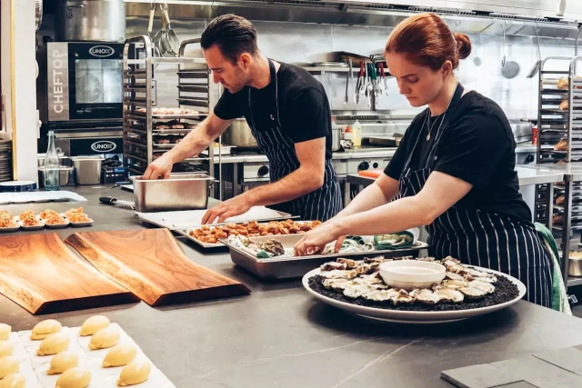 Man and a woman wearing black striped aprons cooking