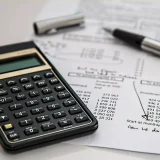 Black calculator near a pen on a white printed paper