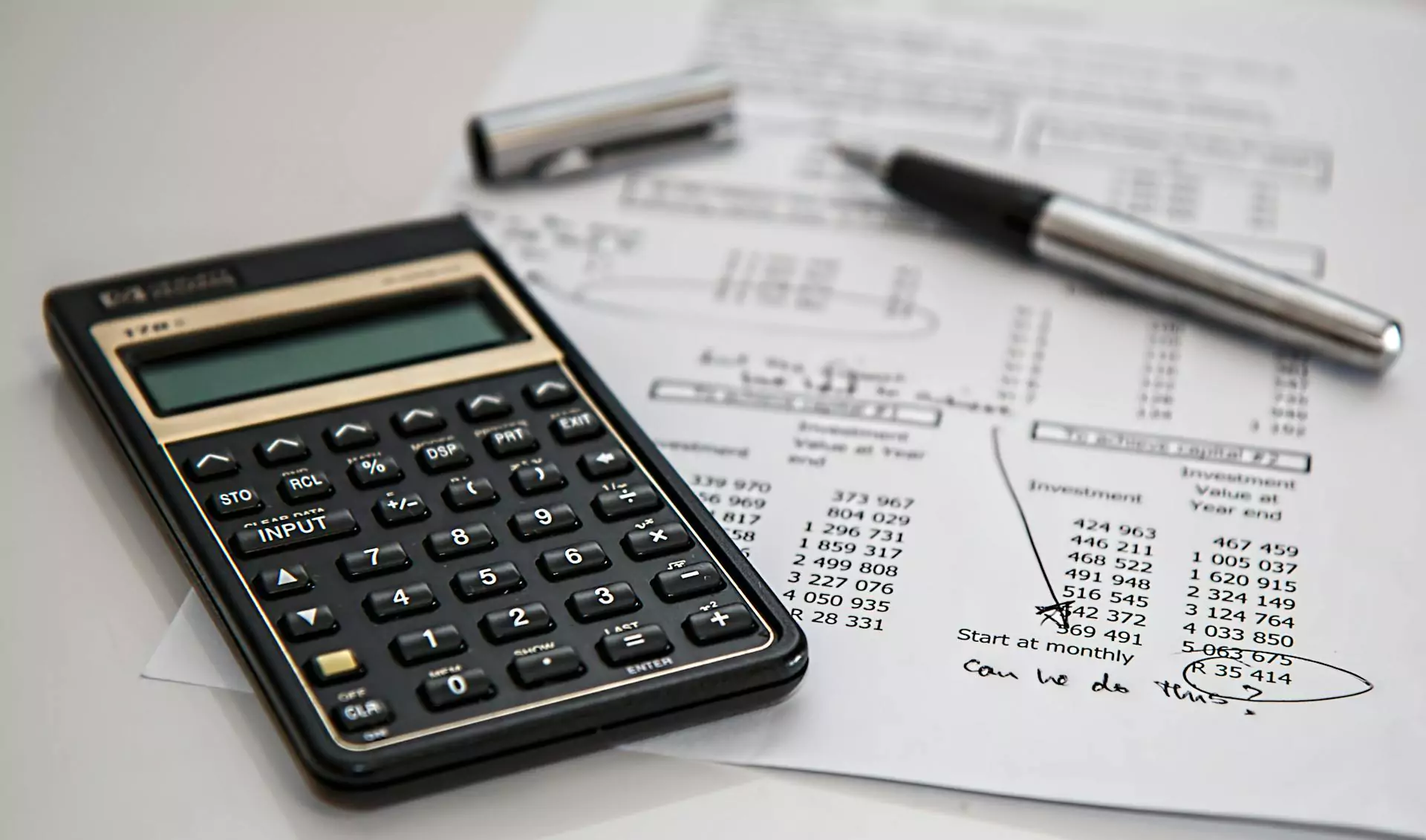 Black calculator near a pen on a white printed paper