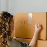 Woman labeling a moving box as fragile while preparing for the "soft move" strategy and organizing relocation