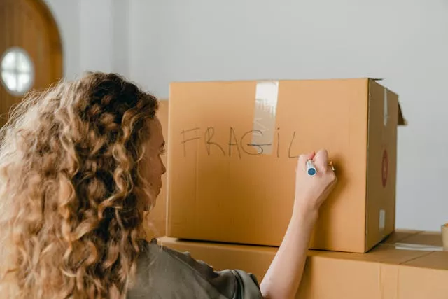 Woman labeling a moving box as fragile while preparing for the "soft move" strategy and organizing relocation