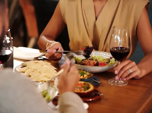 a woman in a restaurant eating a salad and drinking wine